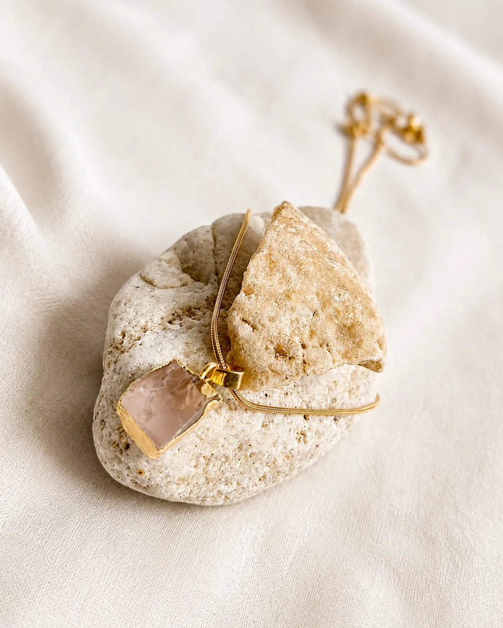 Raw rose quartz gold pendant necklace on stone