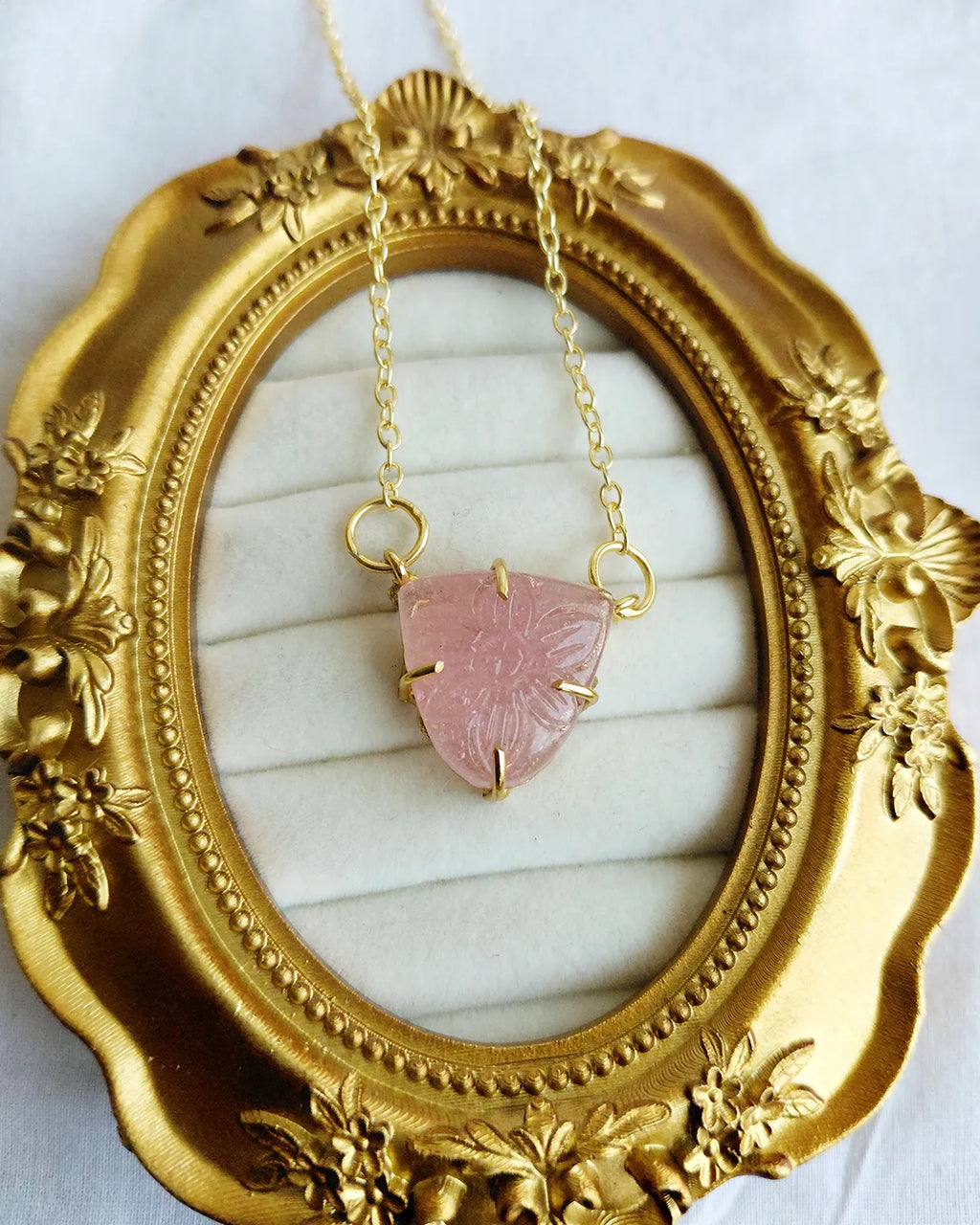 Close-up of pink floral carved triangular pendant on gold-tone chain