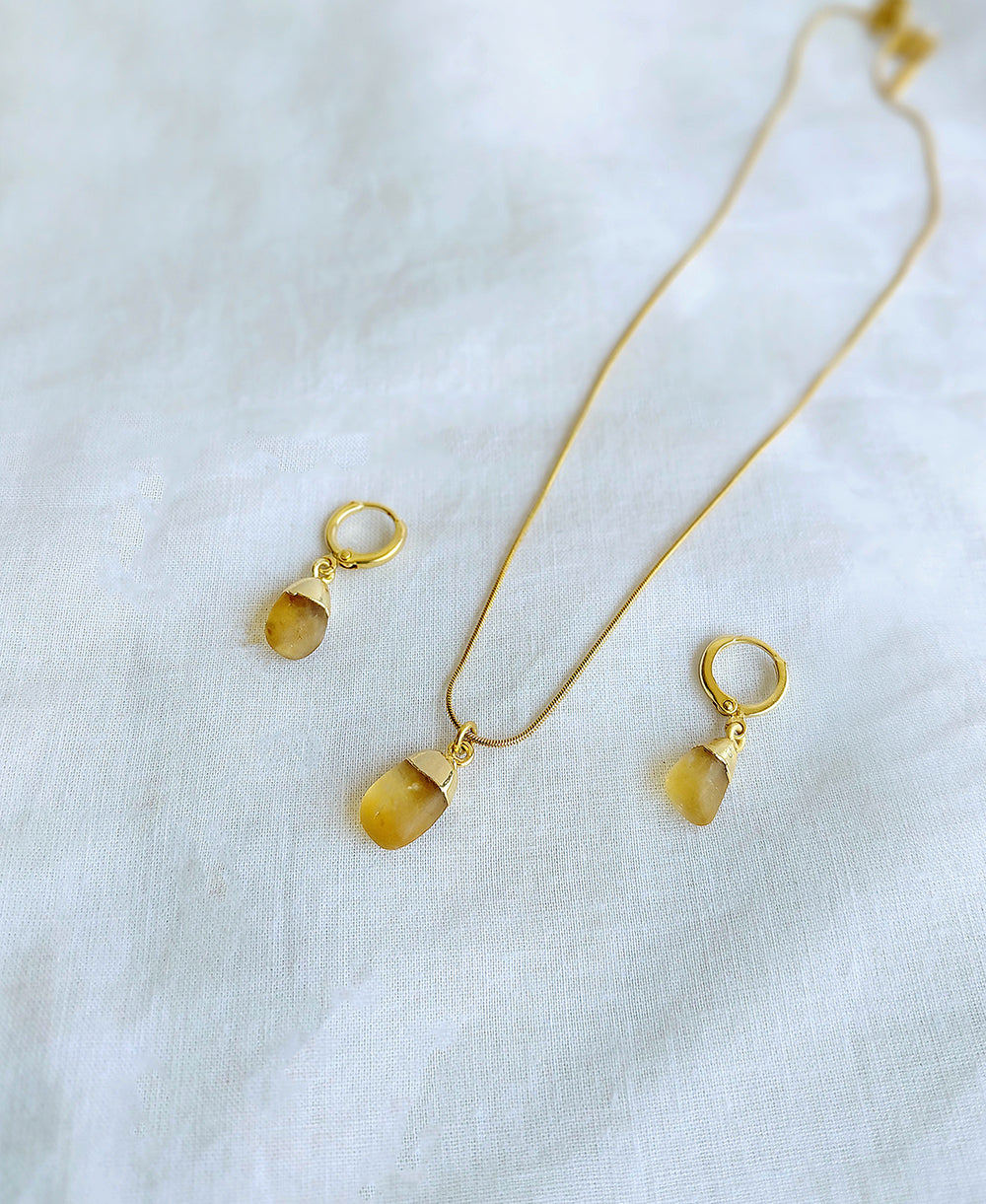 Gold necklace and earrings with yellow gemstones on a white fabric background