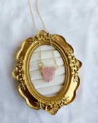 Pink carved stone pendant necklace displayed on ornate gold frame