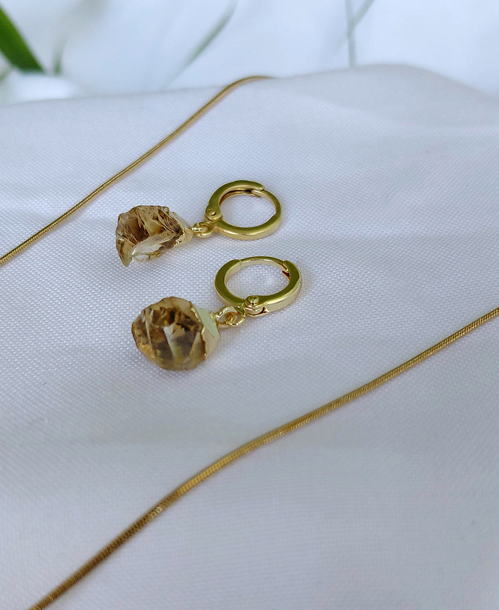Gold earrings with brown gemstones on a white fabric background