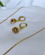 Gold earrings with brown gemstones on a white fabric background