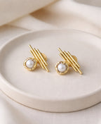 Gold earrings with pearl centers on a beige plate