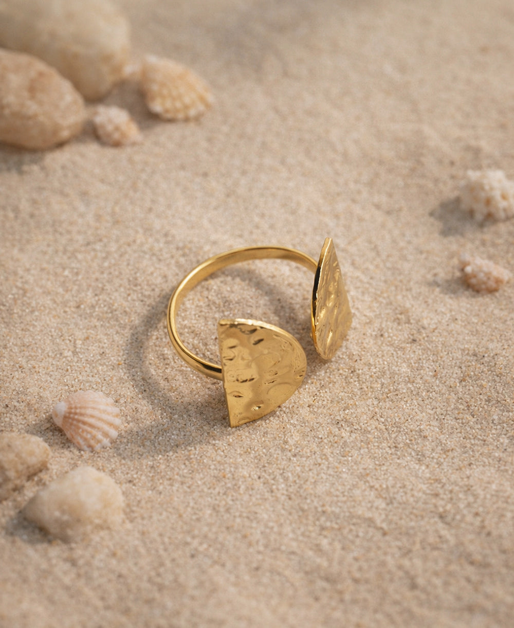 Gold ring with geometric design on a sandy surface with shells
