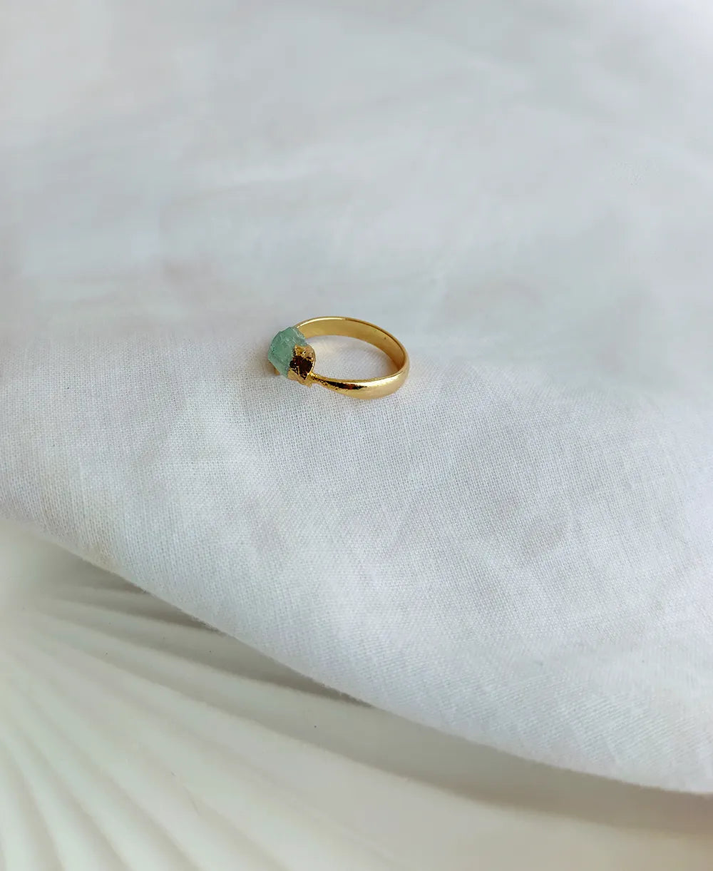 Gold ring with a green gemstone on a white fabric background