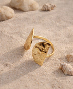 Gold ring with leaf-shaped design on a sandy background with shells