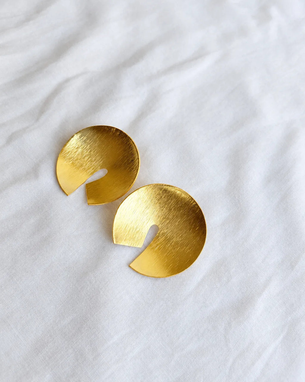 Brushed gold circular disc earrings on white cloth