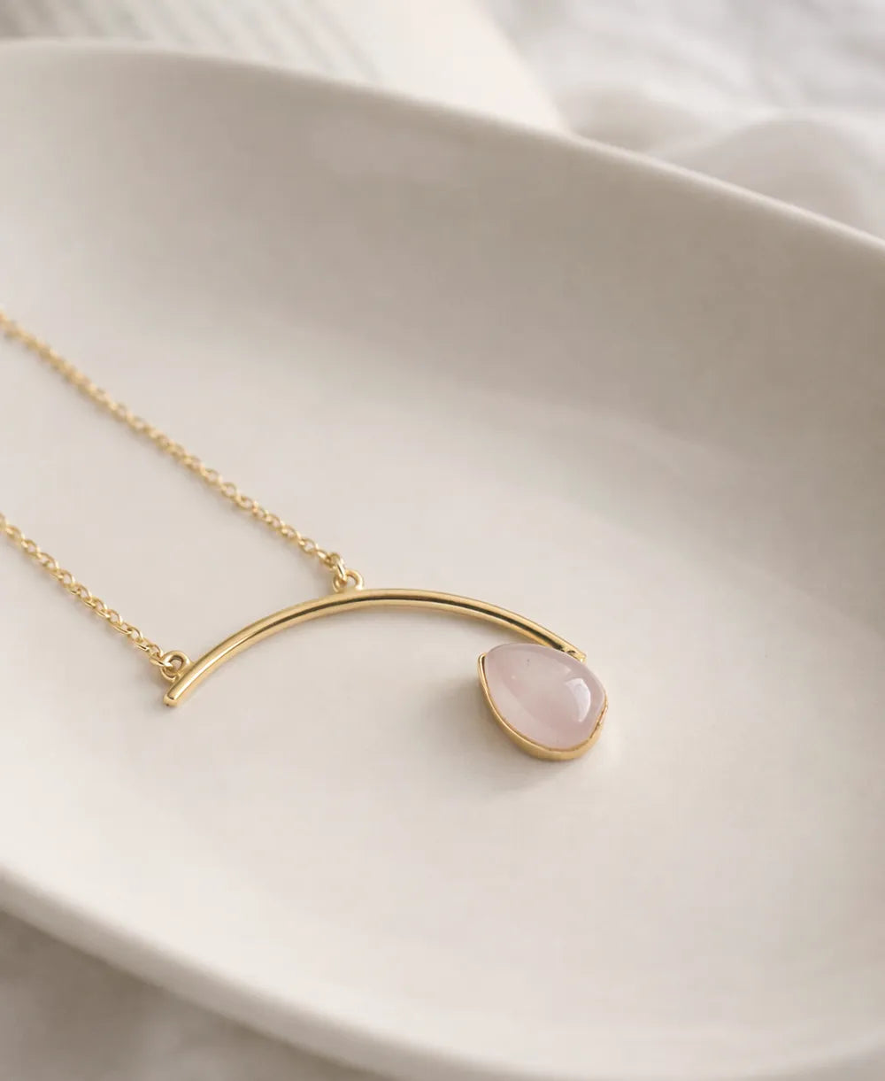 Gold necklace with a pink teardrop pendant on a white dish