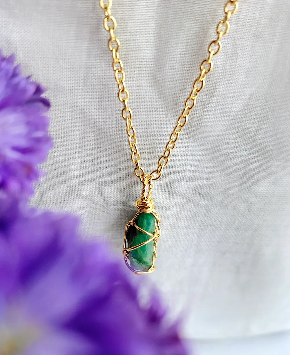 Gold necklace with a green stone pendant on a light fabric background with purple flowers.