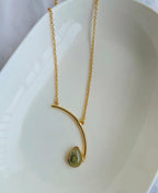 Gold necklace with a green pendant on a white dish