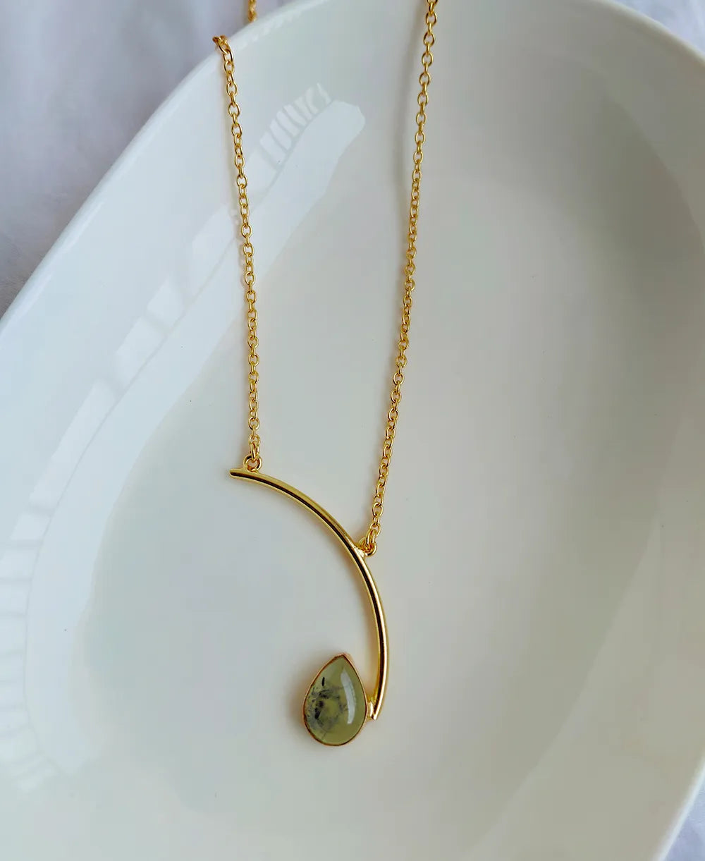 Gold necklace with a green pendant on a white dish