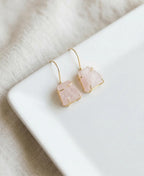 Pair of earrings with pink stone and gold accents on a white surface.