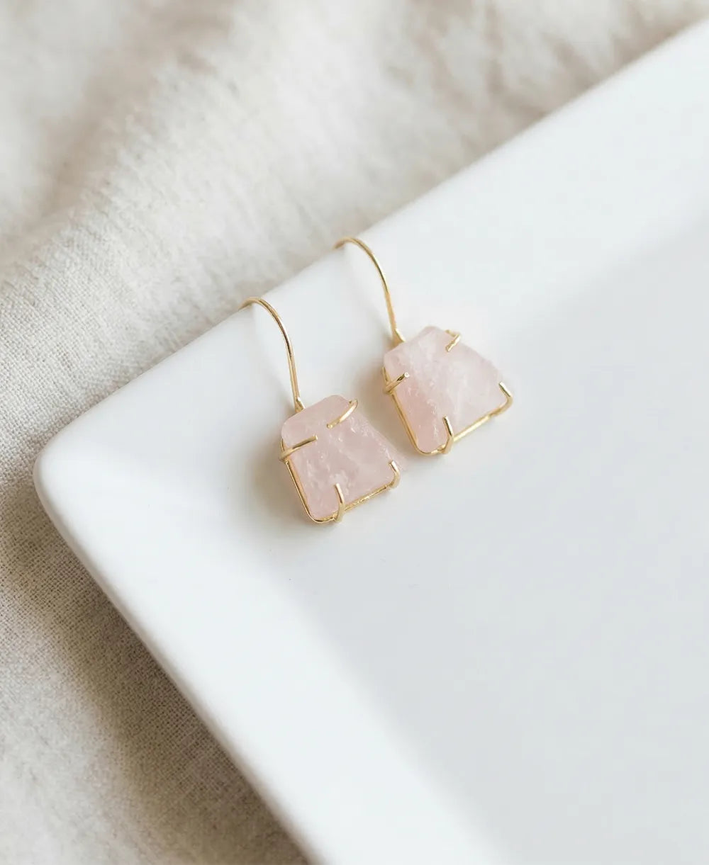 Pair of earrings with pink stone and gold accents on a white surface.