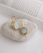 Gold earrings with light blue stones on a white stone surface
