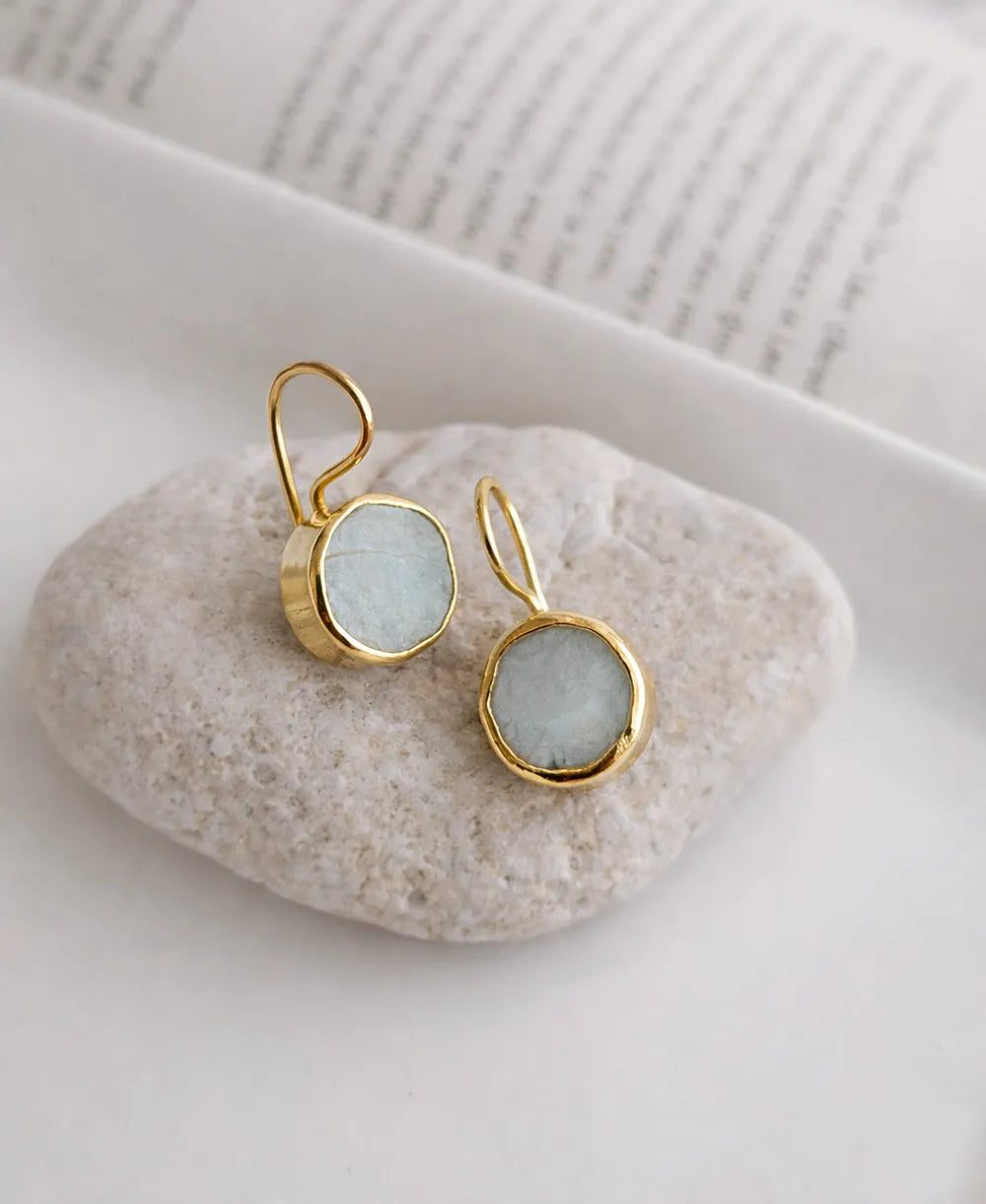 Gold earrings with light blue stones on a white stone surface