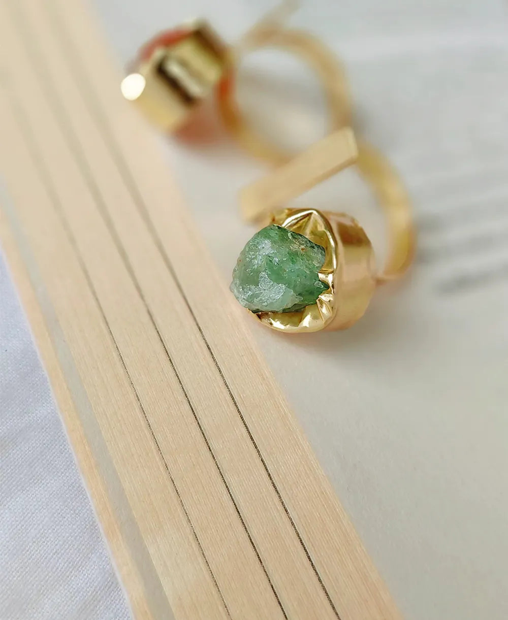 Gold ring with a green gemstone on a light wooden surface
