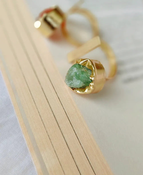 Gold ring with a green gemstone on a light wooden surface