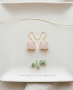 Rose quartz earrings with gold accents on a white plate with eucalyptus leaves.