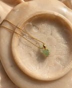 Gold necklace with a green pendant on a textured beige surface