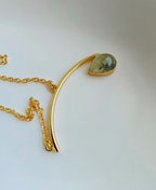 Gold necklace with a teardrop-shaped green gemstone on a white background