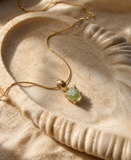 Gold necklace with a green gemstone pendant on a textured beige surface