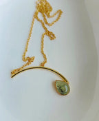 Gold necklace with a green teardrop pendant on a white background