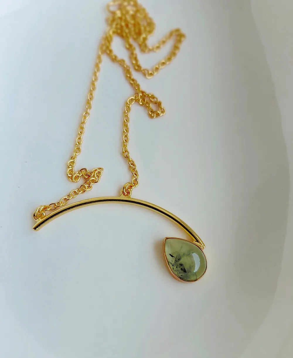 Gold necklace with a green teardrop pendant on a white background