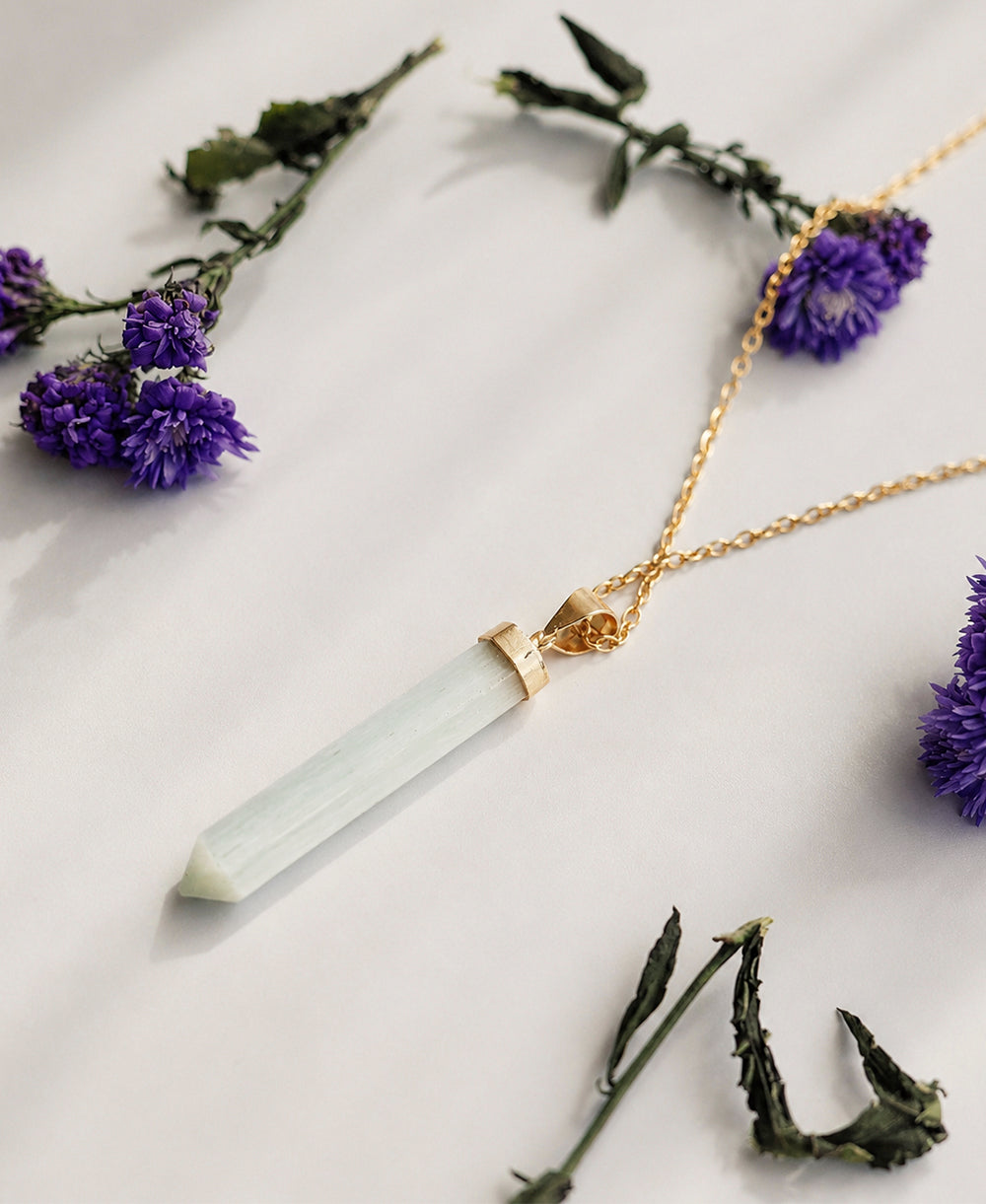 Gold necklace with a clear crystal pendant on a white background with purple flowers.