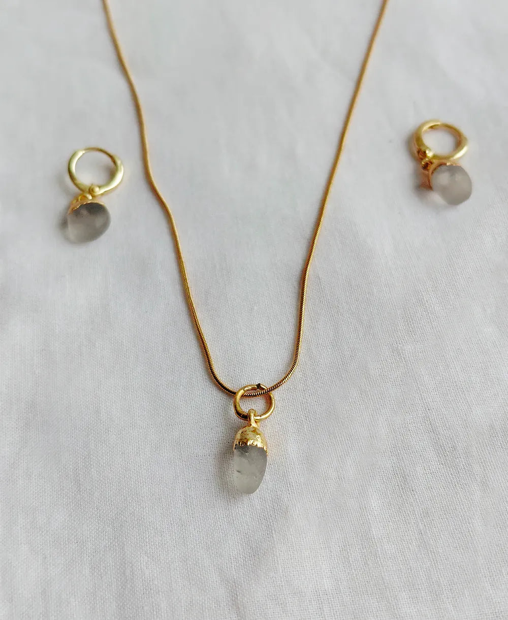 Natural Clear Quartz necklace and matching gold-plated hoop earrings on white fabric.