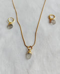 Natural Clear Quartz necklace and matching gold-plated hoop earrings on white fabric.