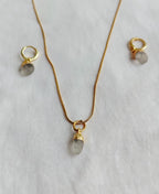 Natural Clear Quartz necklace and matching gold-plated hoop earrings on white fabric.