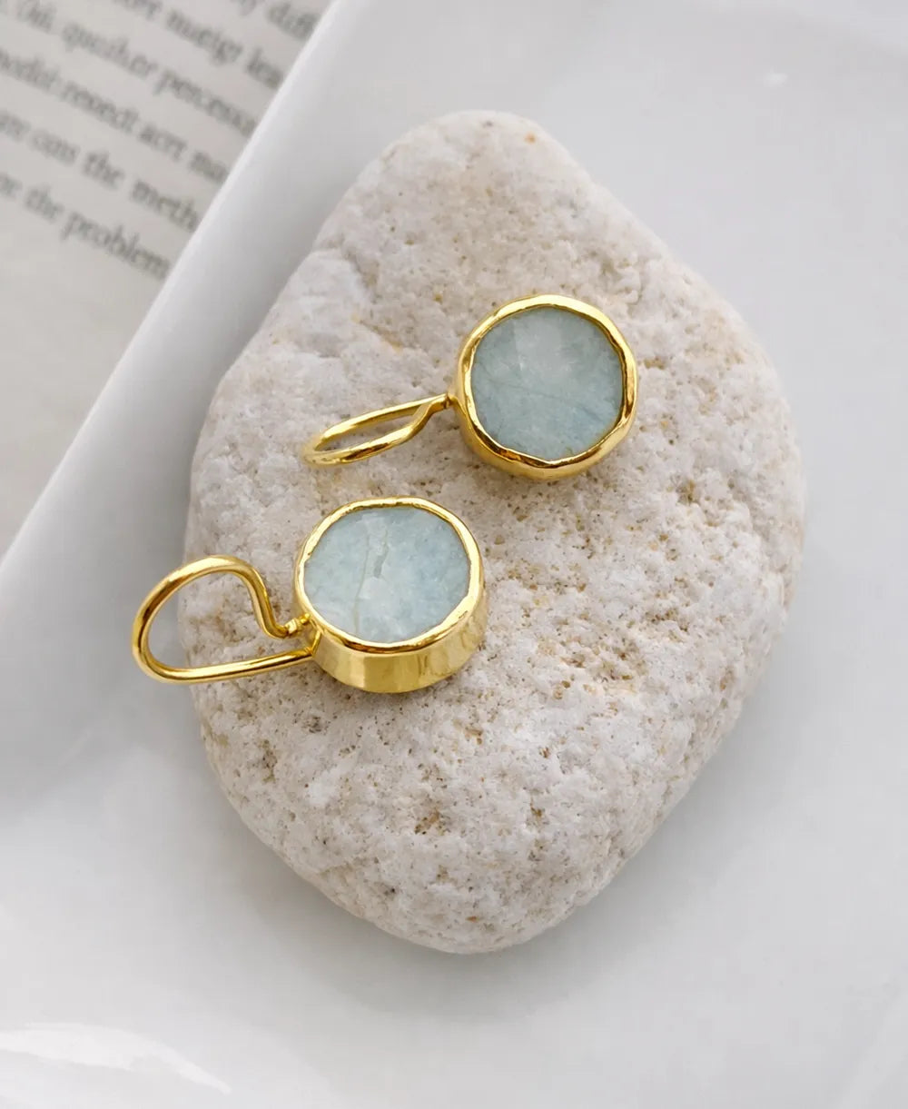 Gold earrings with light blue gemstones on a white stone surface