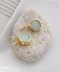 Gold earrings with light blue gemstones on a white stone surface