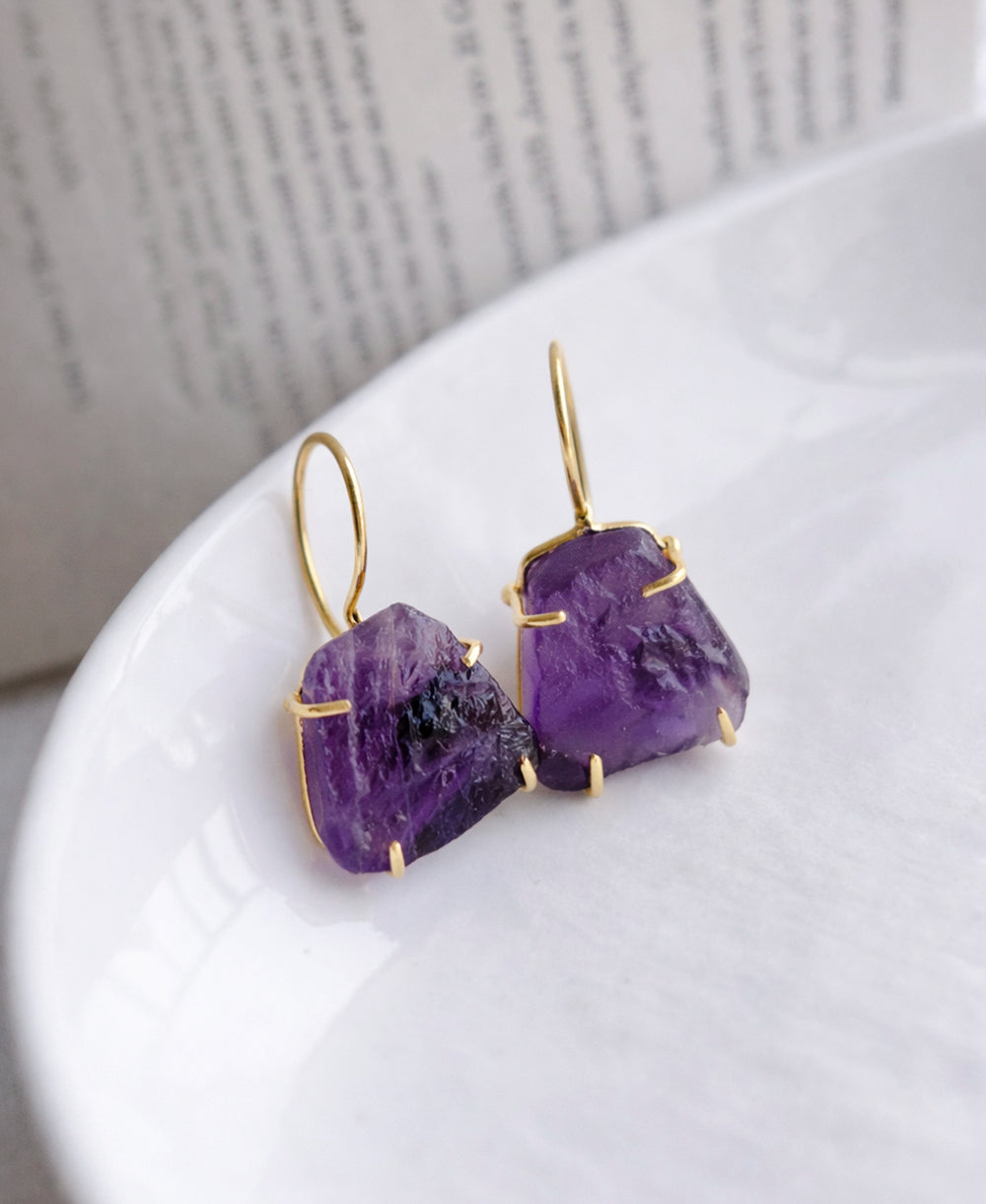 Purple stone earrings with gold accents on a white surface