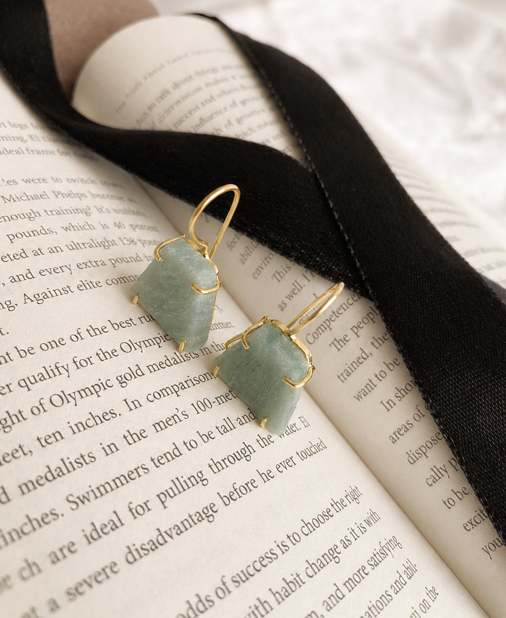 Green earrings on an open book with a black ribbon