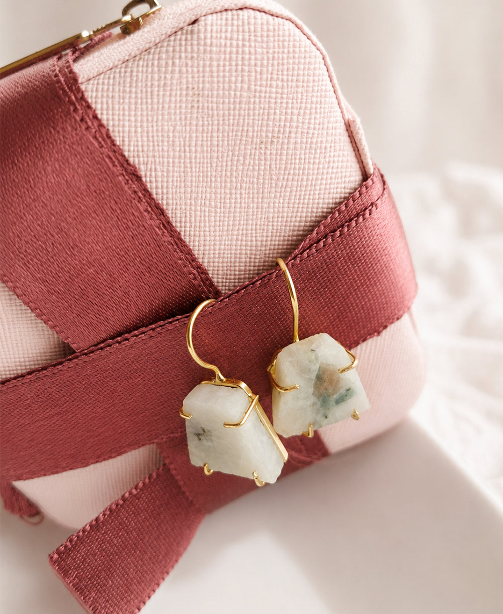 Earrings with green stone drops on gold hooks displayed on a pink pouch.