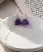 Purple gemstone earrings on a white dish with a book in the background