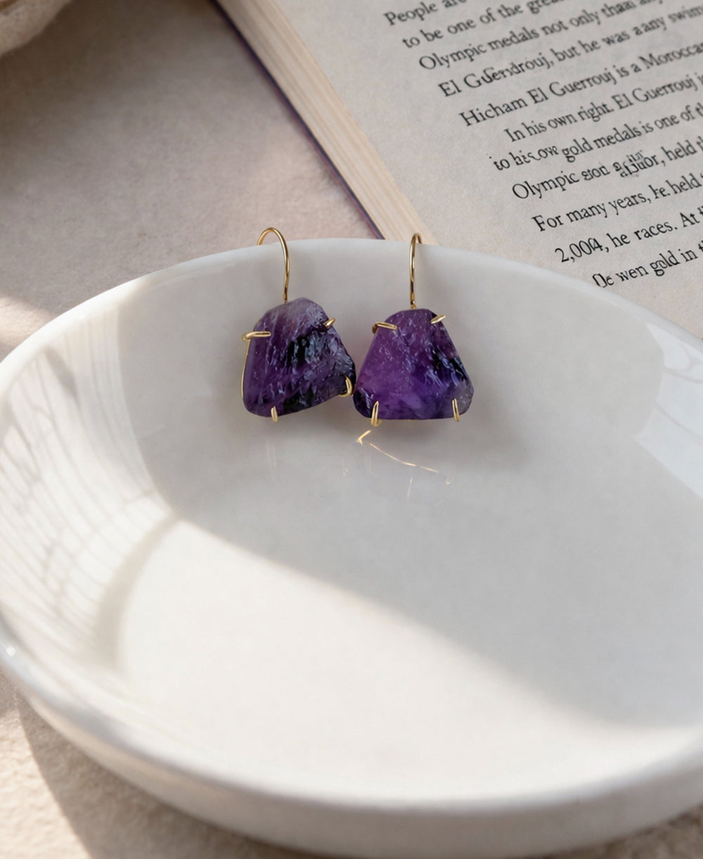 Purple gemstone earrings on a white dish with a book in the background
