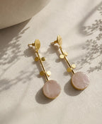 Gold earrings with pink stones on a neutral background