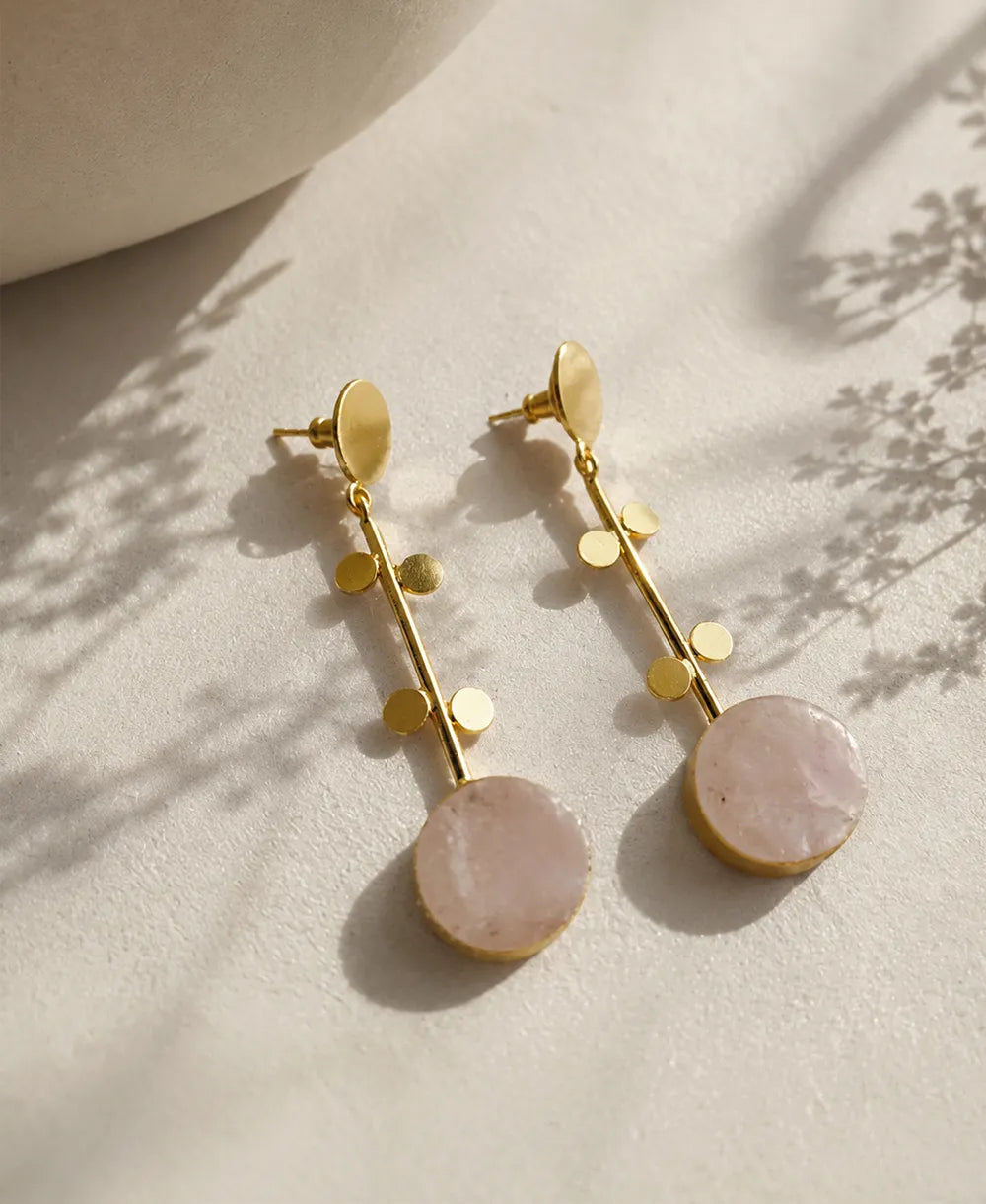Gold earrings with pink stones on a neutral background