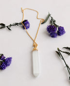 Selenite Aura 18K Gold Necklace with white crystal point pendant and 18K gold-plated chain on a soft floral background
