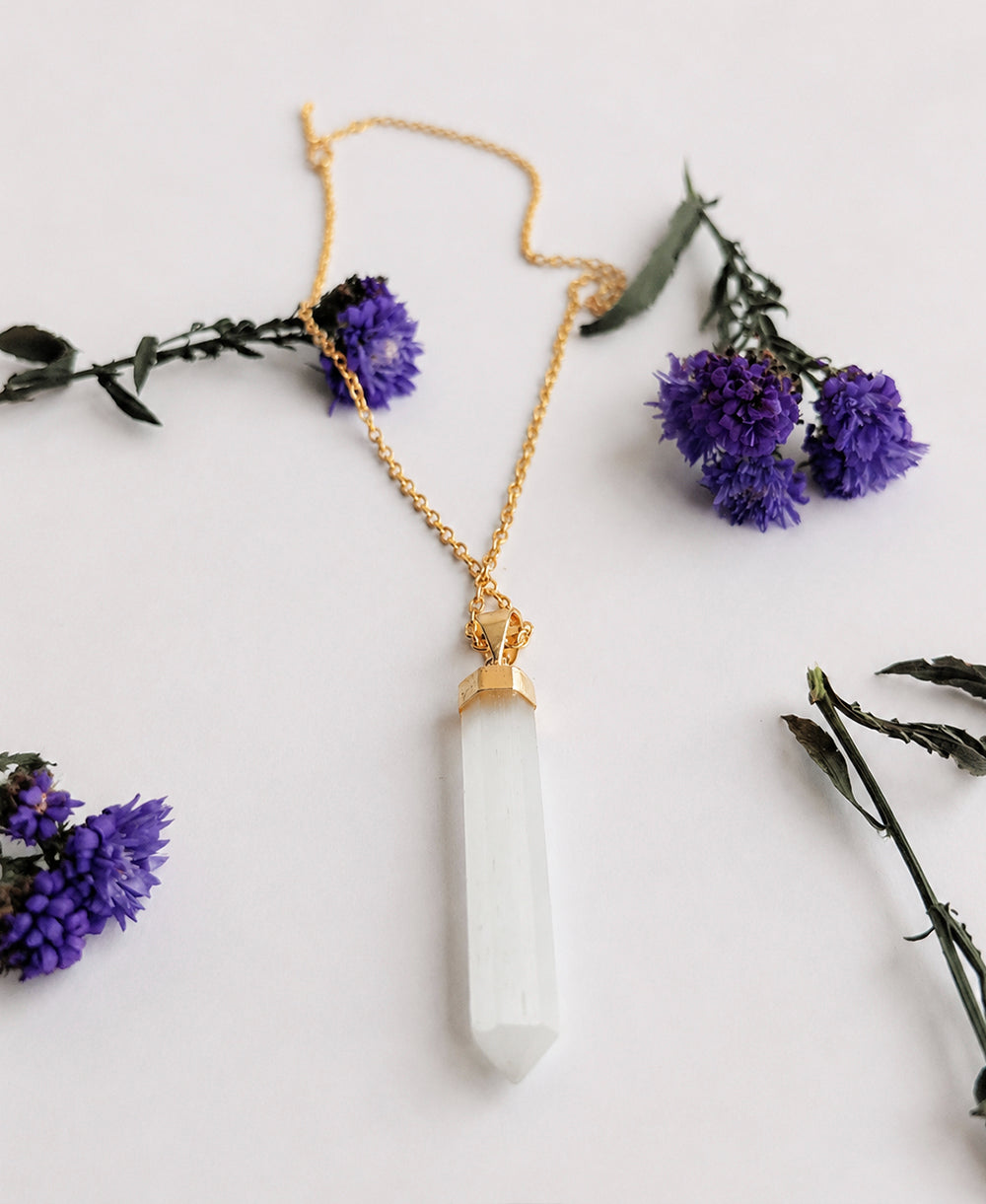 Selenite Aura 18K Gold Necklace with white crystal point pendant and 18K gold-plated chain on a soft floral background