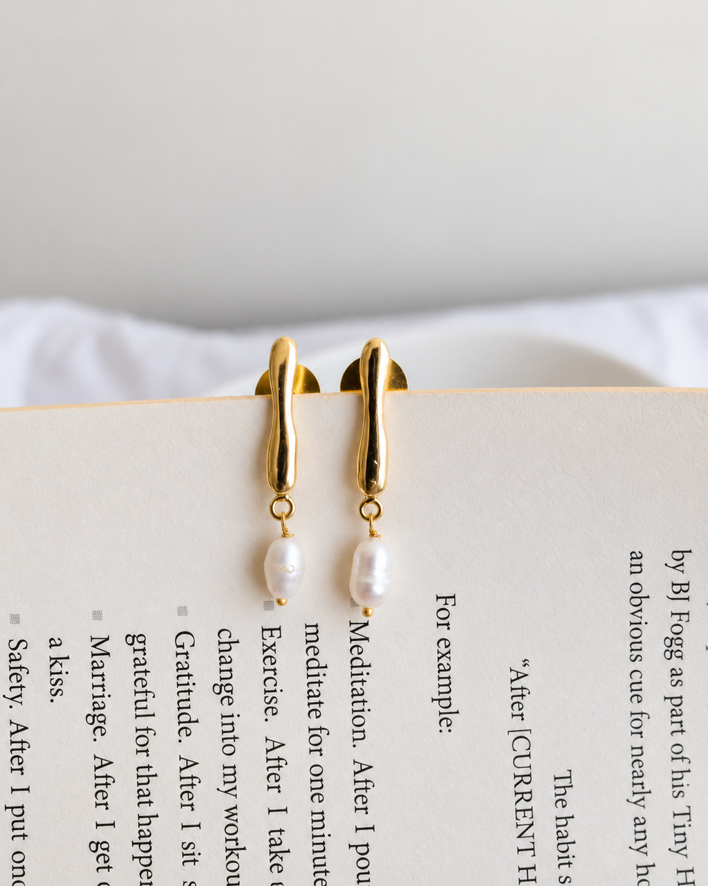Gold pearl drop earrings on open book